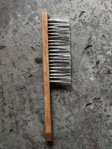 Biborste med trähandtag och naturborst fotograferad ovanifrån mot mörk bakgrund.