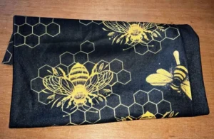 Svart buff med gula bin och bikakemönster, vikt som tubscarf i mjukt tyg.